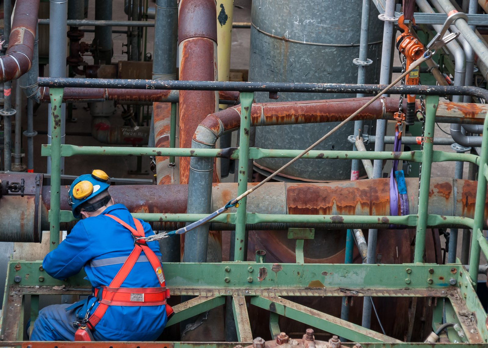 Medewerker in beschermende kleding en veiligheidsharnas bij leidingwerk